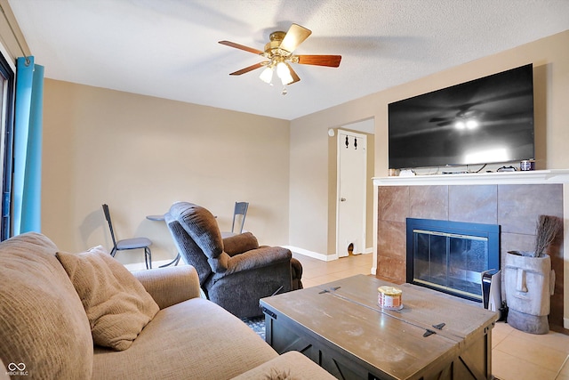 living room with a textured ceiling, ceiling fan, light tile patterned floors, and a fireplace