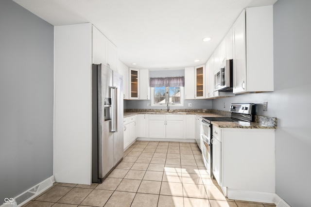 kitchen with white cabinetry, sink, dark stone countertops, light tile patterned floors, and appliances with stainless steel finishes