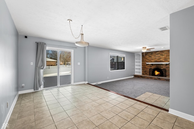 unfurnished living room featuring ceiling fan, light tile patterned flooring, a textured ceiling, and a brick fireplace