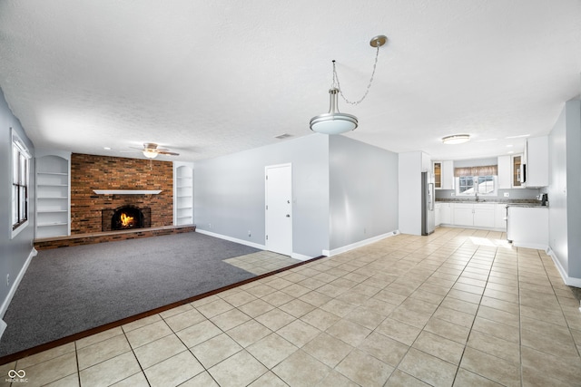 unfurnished living room with a brick fireplace, built in shelves, a textured ceiling, ceiling fan, and light tile patterned floors