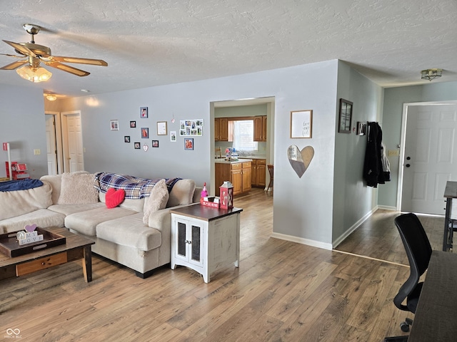 living room featuring ceiling fan, light hardwood / wood-style floors, and a textured ceiling