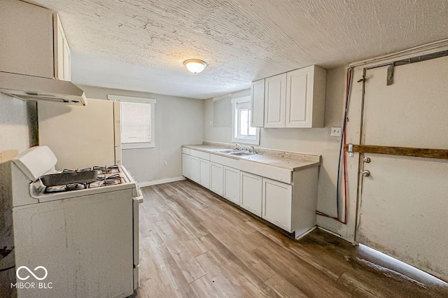 kitchen with gas range gas stove, a textured ceiling, sink, white cabinets, and light hardwood / wood-style floors