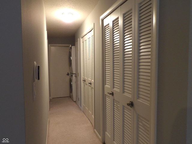 hall with a textured ceiling, light colored carpet, and stacked washer / dryer