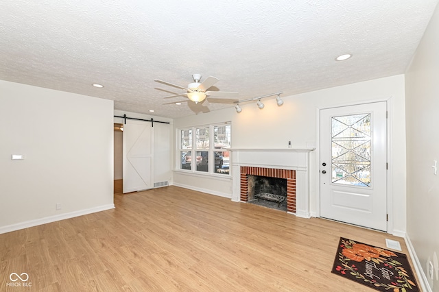 unfurnished living room featuring a fireplace, a textured ceiling, ceiling fan, a barn door, and light hardwood / wood-style floors