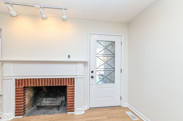 foyer featuring a brick fireplace, light hardwood / wood-style floors, and a textured ceiling