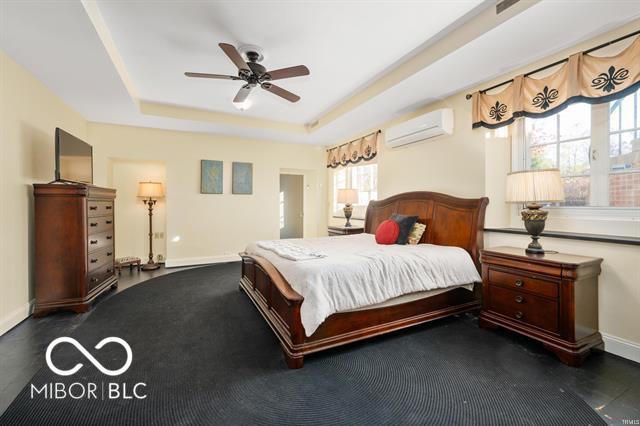 bedroom featuring a raised ceiling, ceiling fan, and an AC wall unit