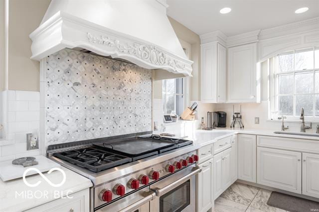 kitchen with range with two ovens, sink, custom range hood, tasteful backsplash, and white cabinetry