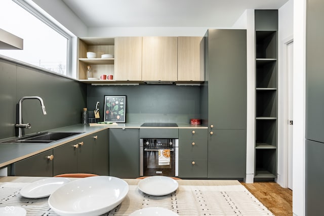 kitchen with black electric stovetop, oven, sink, built in features, and light wood-type flooring