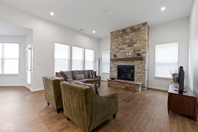 living area featuring a wealth of natural light, recessed lighting, dark wood-type flooring, and a stone fireplace