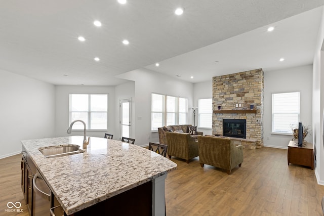 kitchen with an island with sink, light wood-style flooring, a sink, and a stone fireplace