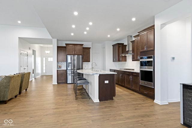 kitchen featuring dark brown cabinetry, beverage cooler, a kitchen breakfast bar, wall chimney range hood, and appliances with stainless steel finishes