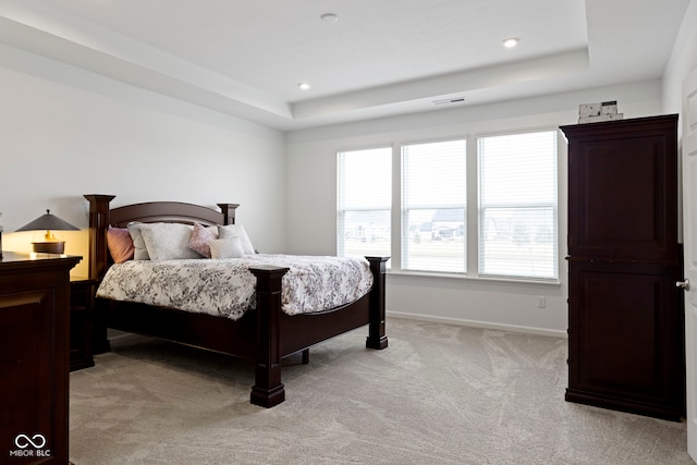 bedroom with a tray ceiling, recessed lighting, light colored carpet, visible vents, and baseboards