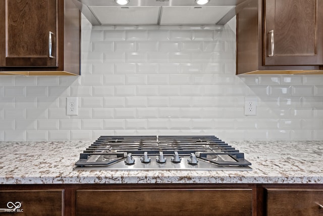 kitchen with tasteful backsplash, wall chimney exhaust hood, stainless steel gas stovetop, and dark brown cabinets