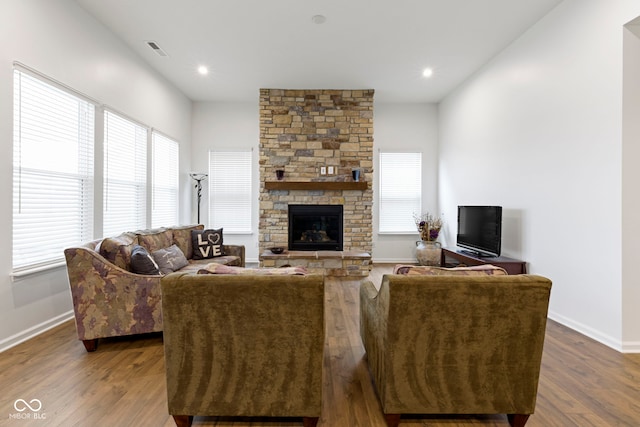 living area with a stone fireplace, dark wood-style flooring, visible vents, and baseboards