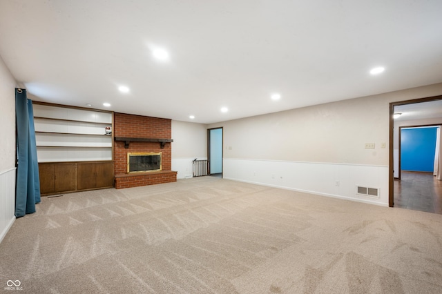 unfurnished living room with built in features, light colored carpet, and a brick fireplace