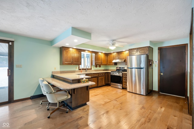 kitchen featuring ceiling fan, stainless steel appliances, light hardwood / wood-style flooring, kitchen peninsula, and a breakfast bar area