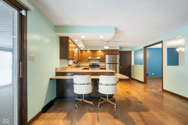 kitchen with kitchen peninsula, stainless steel appliances, ceiling fan, sink, and a breakfast bar area