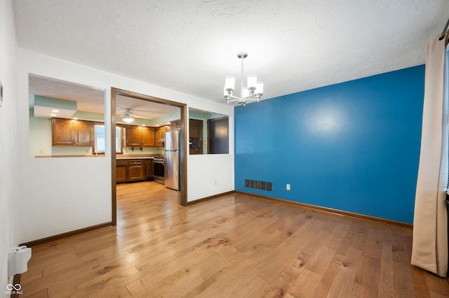 unfurnished dining area featuring a textured ceiling, light wood-type flooring, and an inviting chandelier