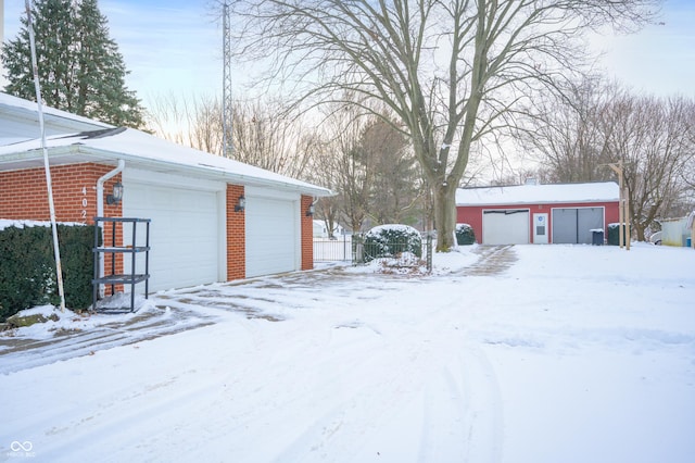 yard layered in snow featuring an outbuilding and a garage