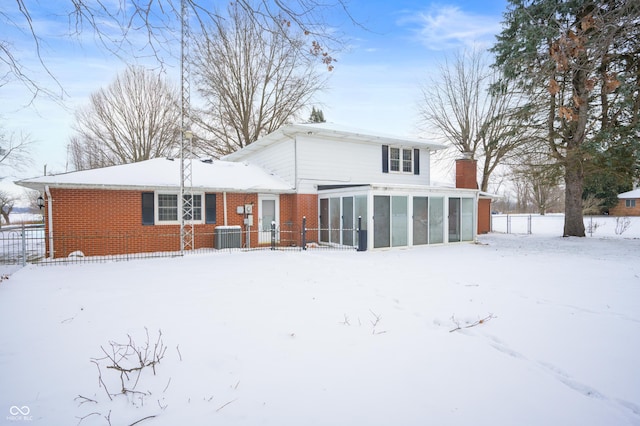 snow covered property with a sunroom and central AC