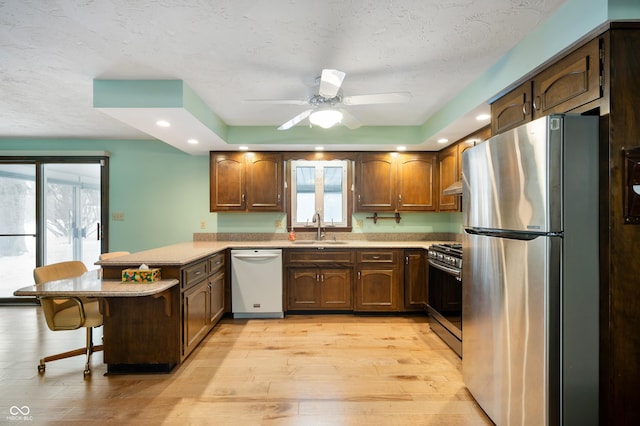 kitchen featuring light hardwood / wood-style flooring, a textured ceiling, appliances with stainless steel finishes, a kitchen bar, and kitchen peninsula