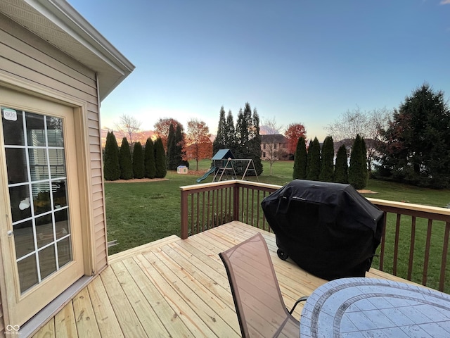 deck at dusk featuring a playground, a lawn, and a grill