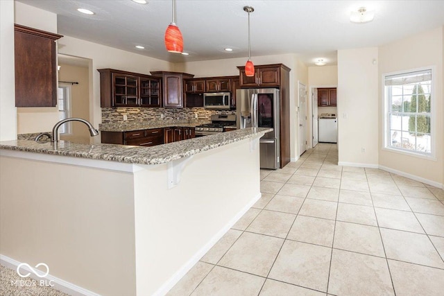 kitchen with pendant lighting, dark brown cabinets, light stone counters, kitchen peninsula, and stainless steel appliances