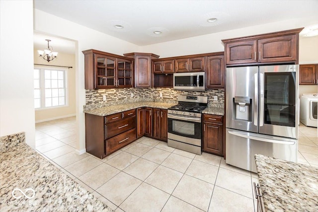 kitchen featuring backsplash, an inviting chandelier, light stone countertops, washer / dryer, and stainless steel appliances