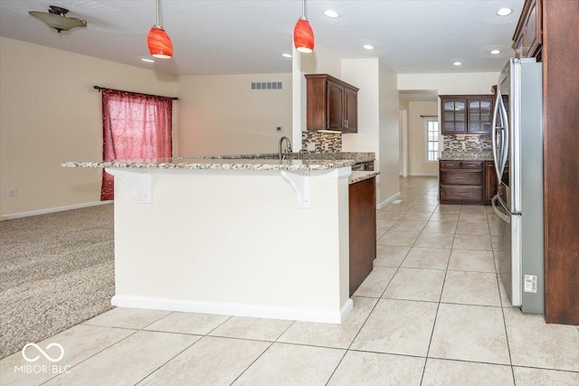 kitchen featuring kitchen peninsula, pendant lighting, a breakfast bar, and stainless steel refrigerator