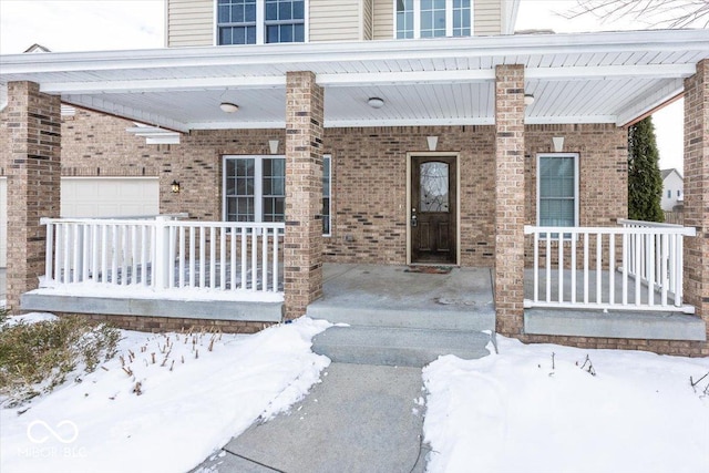 snow covered property entrance with a porch and a garage