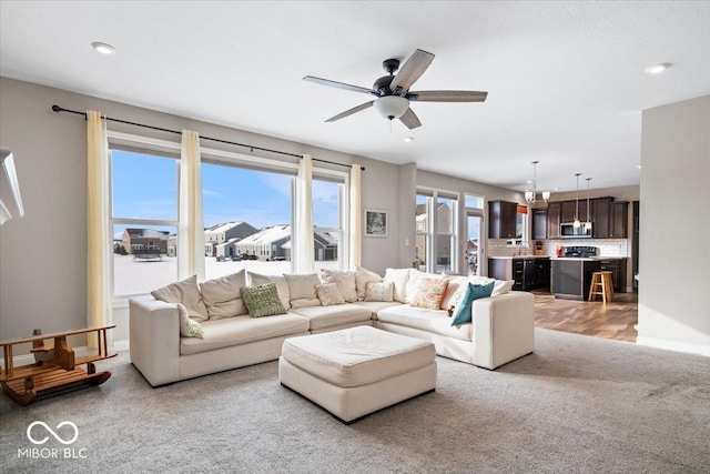 living room featuring light carpet and ceiling fan with notable chandelier