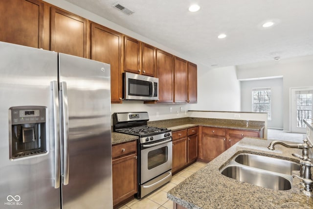 kitchen featuring dark stone countertops, sink, light tile patterned floors, and appliances with stainless steel finishes