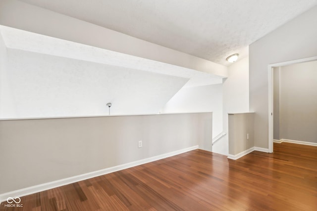 additional living space featuring dark hardwood / wood-style floors, a textured ceiling, and vaulted ceiling