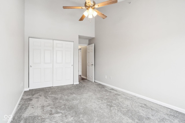 unfurnished bedroom featuring ceiling fan, a closet, carpet floors, and a high ceiling