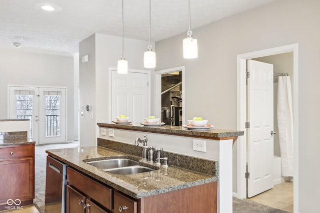 kitchen featuring french doors, stainless steel dishwasher, a kitchen island with sink, sink, and decorative light fixtures