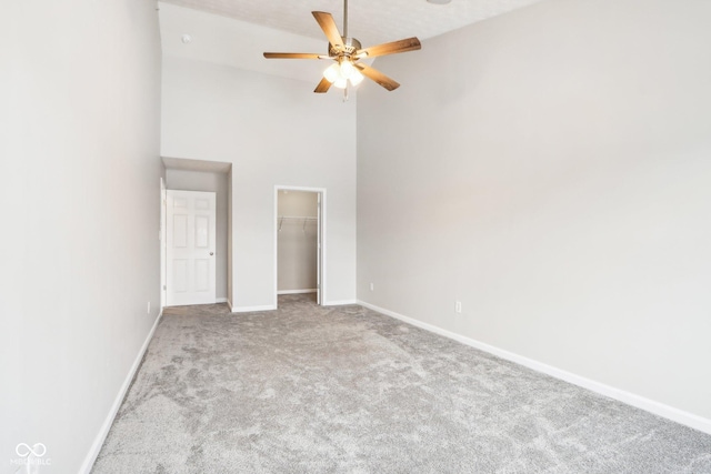 unfurnished bedroom featuring a walk in closet, light colored carpet, high vaulted ceiling, and ceiling fan