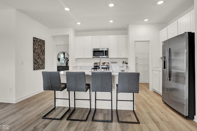 kitchen featuring light hardwood / wood-style floors, a breakfast bar, a kitchen island with sink, appliances with stainless steel finishes, and white cabinets