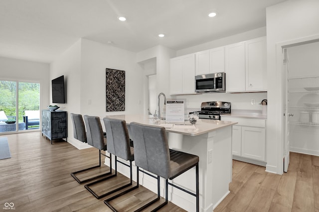 kitchen with a kitchen bar, a center island with sink, appliances with stainless steel finishes, light wood-type flooring, and white cabinets