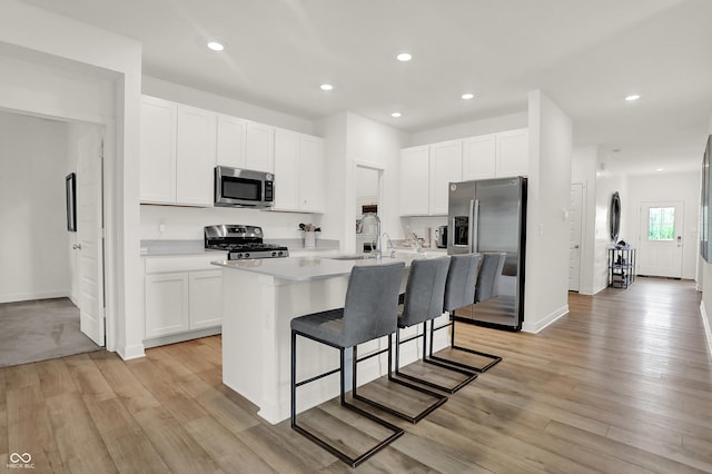 kitchen featuring white cabinetry, stainless steel appliances, a kitchen island with sink, a breakfast bar, and sink