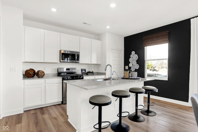 kitchen with appliances with stainless steel finishes, light wood-type flooring, sink, white cabinets, and an island with sink