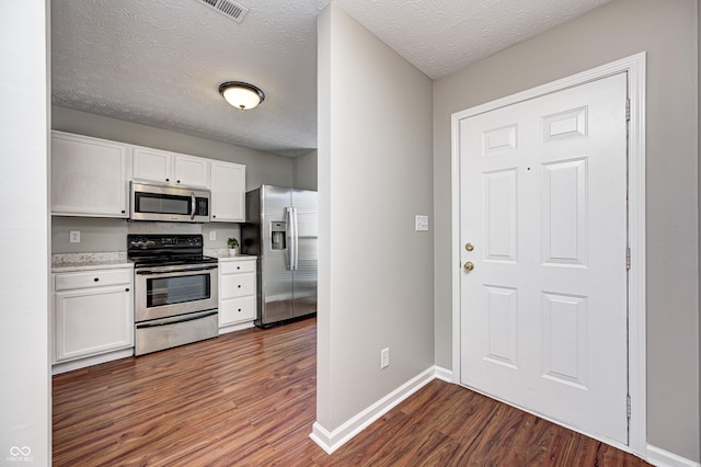 kitchen with white cabinets, appliances with stainless steel finishes, a textured ceiling, and dark hardwood / wood-style floors