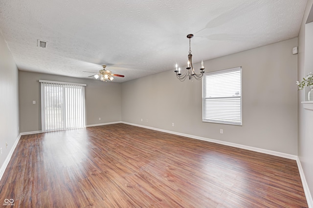 empty room featuring a textured ceiling, a healthy amount of sunlight, ceiling fan with notable chandelier, and wood-type flooring