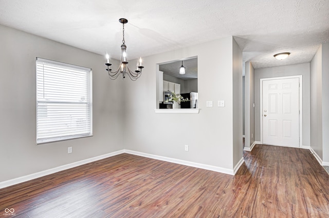 empty room with a textured ceiling, dark hardwood / wood-style flooring, and a notable chandelier