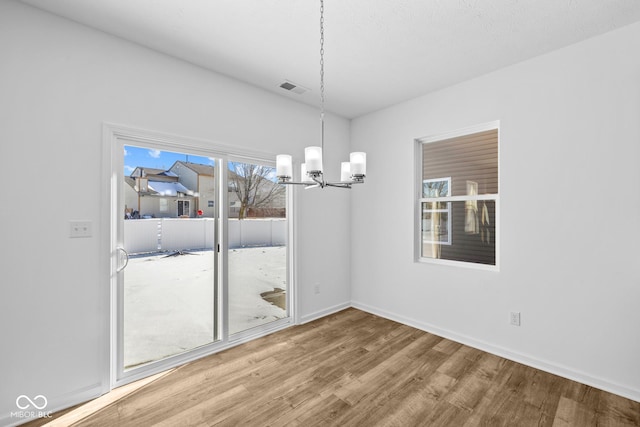 unfurnished dining area with baseboards, wood finished floors, visible vents, and a notable chandelier