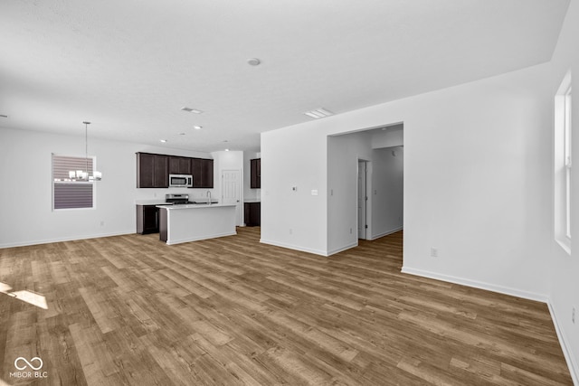 unfurnished living room featuring a chandelier, a sink, wood finished floors, and baseboards