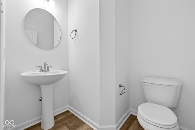 half bath featuring wood finished floors, toilet, and baseboards