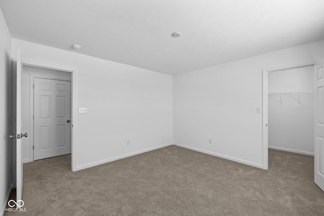 unfurnished bedroom with a textured ceiling, baseboards, a spacious closet, a closet, and carpet