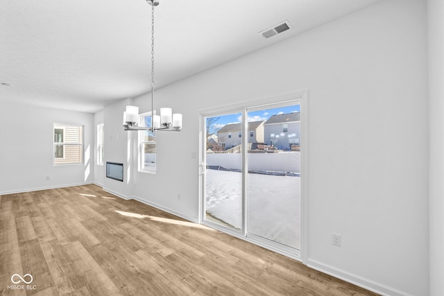 unfurnished dining area featuring a fireplace, visible vents, wood finished floors, a chandelier, and baseboards