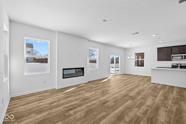 unfurnished living room featuring a glass covered fireplace, visible vents, light wood finished floors, and an inviting chandelier