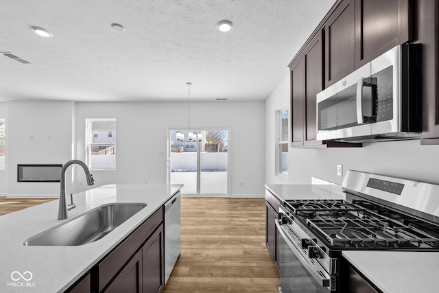 kitchen featuring light wood finished floors, visible vents, appliances with stainless steel finishes, a sink, and dark brown cabinetry